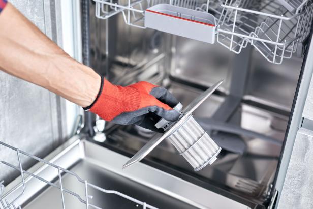 Concept maintenance service of home appliances. Worker cleans filter in dishwasher. Male repairman checking food residue filters.
