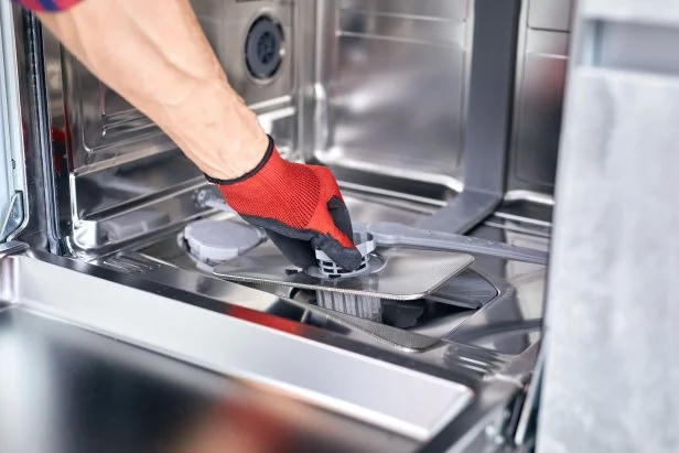 Concept maintenance service of home appliances. Worker cleans filter in dishwasher. Male repairman checking food residue filters.