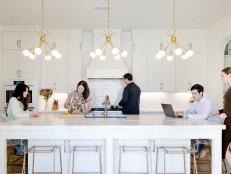 A family gathers in a white kitchen with gold chandeliers.