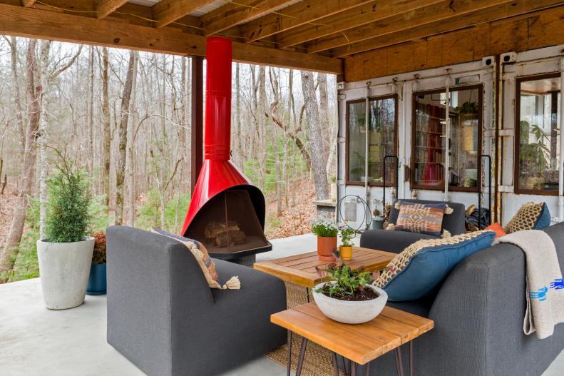 A covered porch with outdoor seating and a freestanding red fireplace 