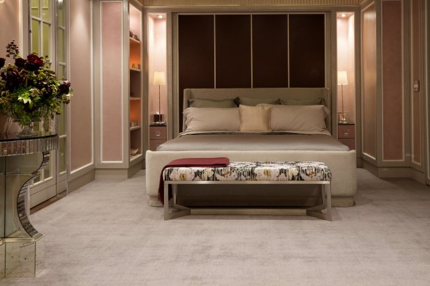 Pink bedroom with upholstered bed, floral bench and pale carpeting.