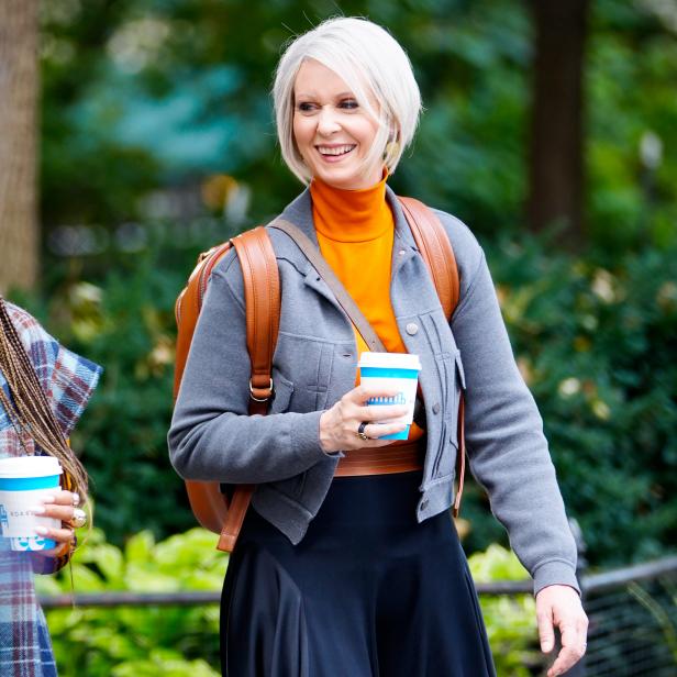 Woman with white bob and leather backpack holding a coffee.