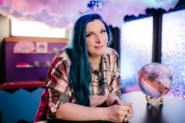 Woman Smiles to Camera Near Crystal Ball and Clouds Above Desk