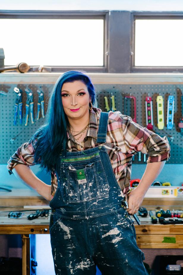 Woman in Overalls Smiles to Camera with Tools Hanging Behind Her