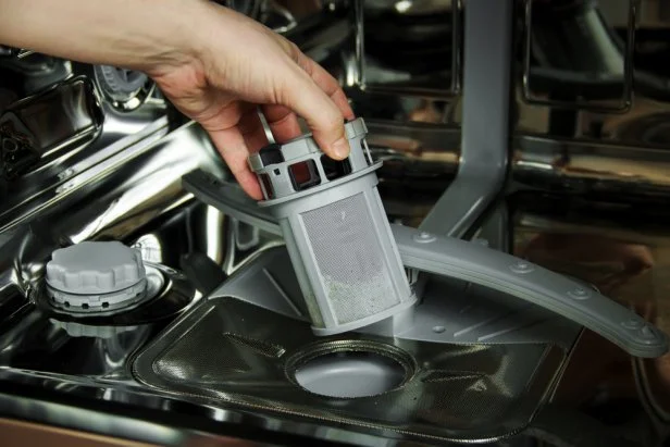 man cleans the filter in the dishwasher. Maintenance of home appliances.