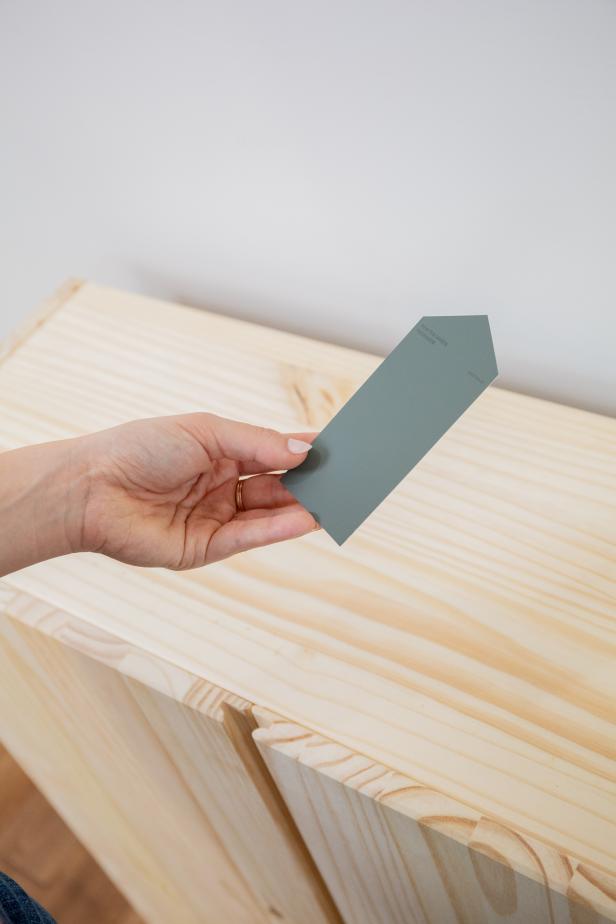 A Woman Holding a Paint Chip Above an Unfinished Cabinet