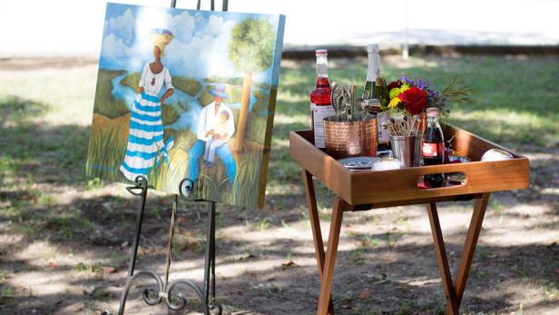 A painting sits on an outdoor easel next to a tray table. 