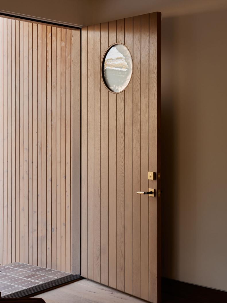 An open wooden front door with vertical lines and a circular window