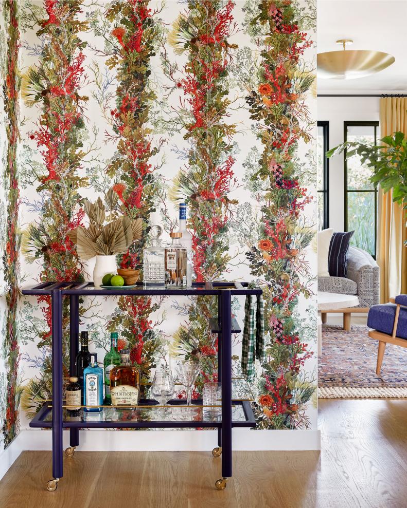 A blue bar cart in a corner with red and blue floral vine wallpaper.