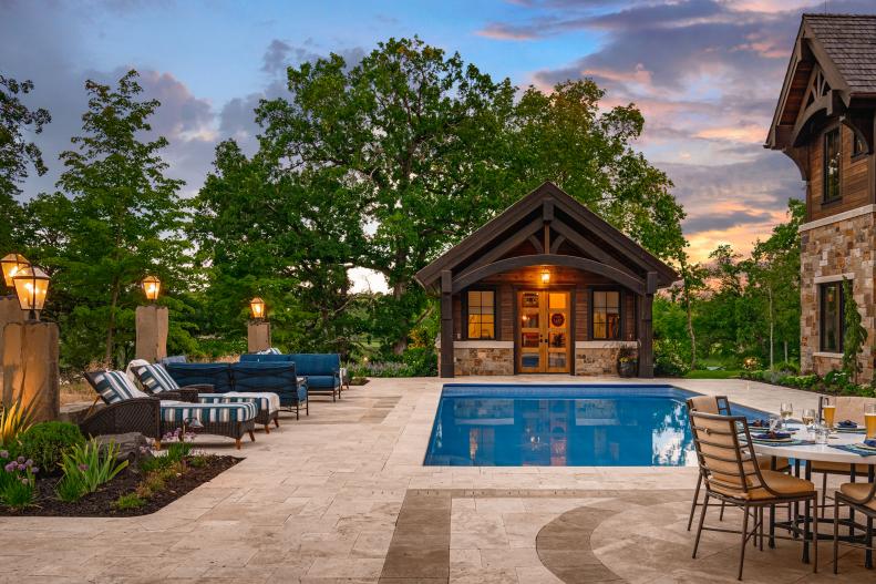 A backyard with a poolhouse, pool, and patio.