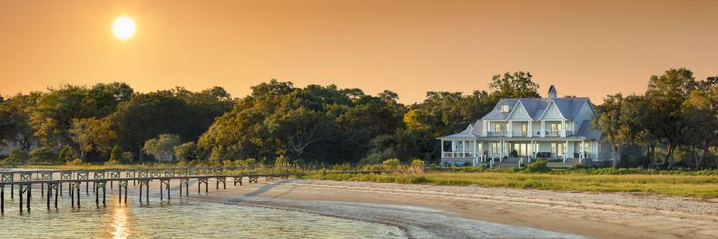 Wide photo with a beach house and pier at sunset.