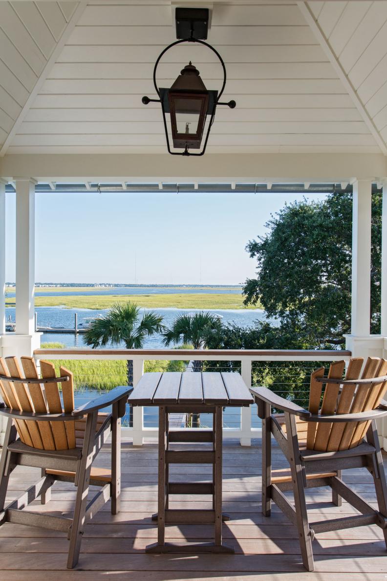 Two Adirondack-style chairs on a porch overlooking water. 