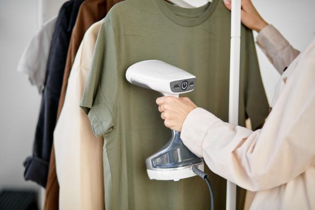 Woman using steaming iron to ironing casual t-shirt at home. Girl doing stream vapor iron for press clothes in hand. Cropped female doing household chores, housewife using modern device for ironing