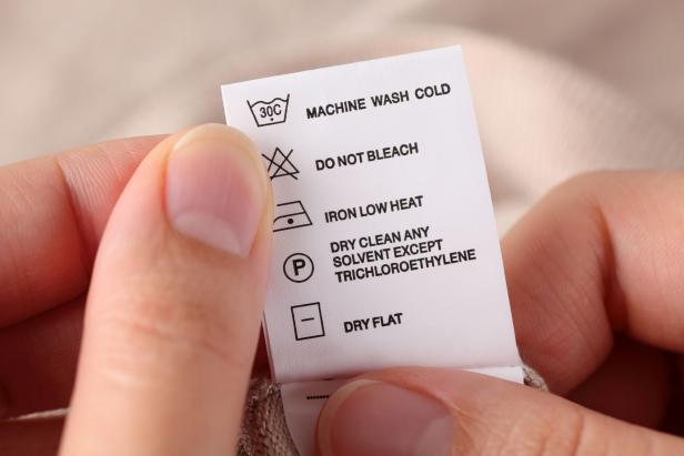 Woman's hands holding clothes label with cleaning instructions.