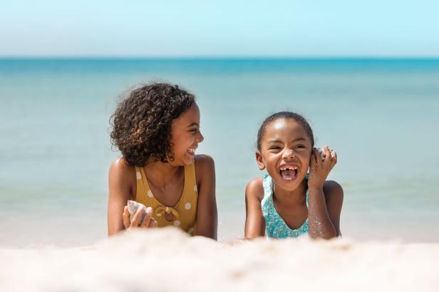 Two little girls lying on the sand and laughing with the Gulf of Mexico in the background.