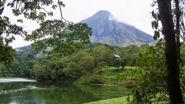 A view of a lake and trees in Costa Rica with the Arenal Volcano in the background.