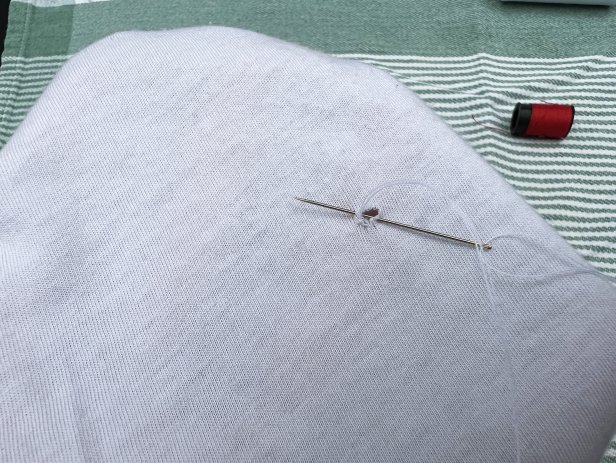 Using a needle and thread to sew a small hole in a white cotton t-shirt.