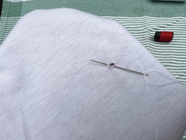 Using a needle and thread to sew a small hole in a white cotton t-shirt.