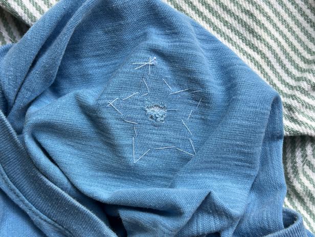 Sewing a star-shaped patch to cover a hole in a t-shirt.