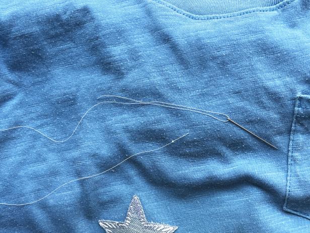 Sewing a star-shaped patch to cover a hole in a t-shirt.