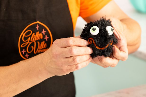 Step 10 of creating the spider hand puppet is to use a craft knife to cut shallow guide holes in the head above the mouth so the toothpicks attached to the eyes can be pressed into the puppet's head.