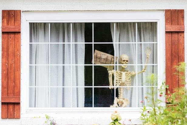 Skeleton inside large window with a sign that says "help."