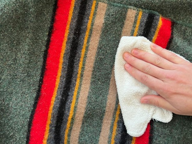 Hand presses a white cloth onto a stain on a Pendleton blanket.