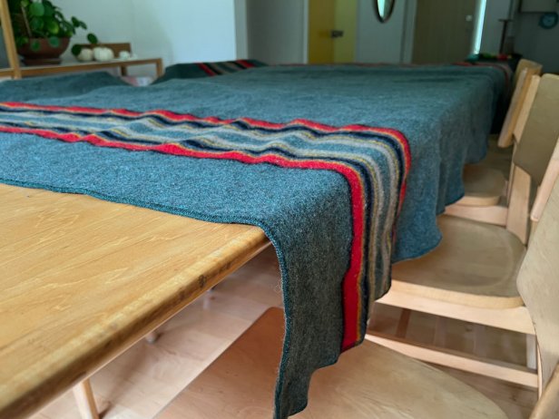 A Pendleton wool blanket dries on a light wood table.
