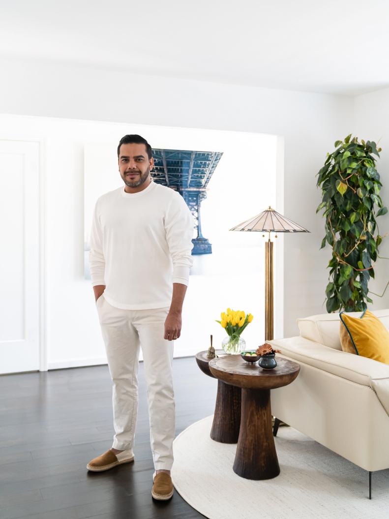 Man with black hair and goatee standing in bright living room. 