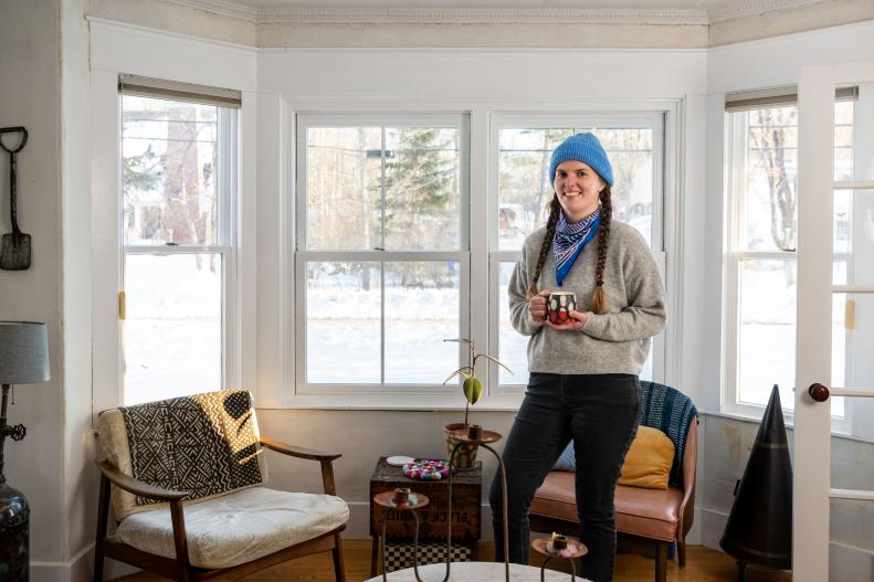 Woman in Blue Beanie Holds Coffee Mug in Bright Living Room