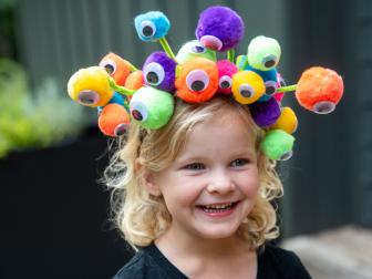 Girl wearing a colorful headband covered with pom-poms and google eyes.