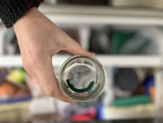 A glass container filled with candle wax is placed in a freezer.