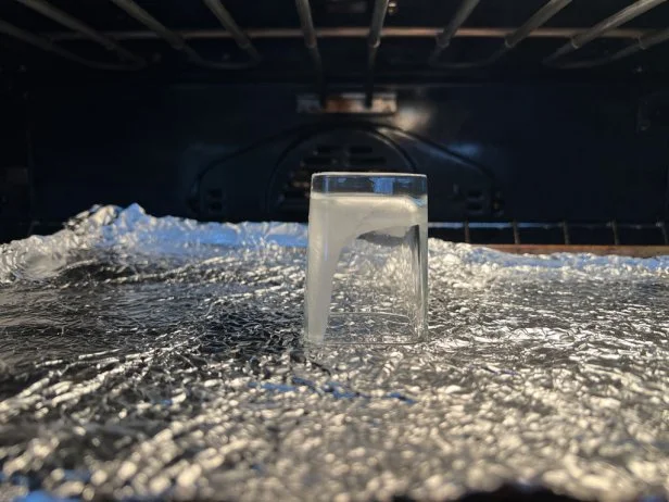 A glass votive holder dripping melted wax in an oven.