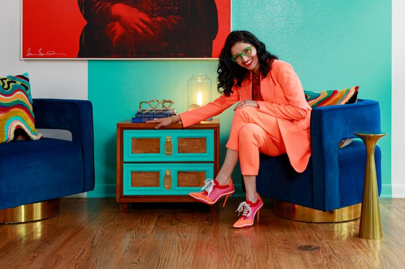 Woman in peach suit displaying teal dresser below red painting. 