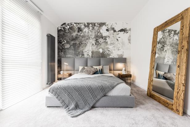King-size bed with gray square headboard, large rustic wooden mirror and textured wall in trendy minimalist apartment 