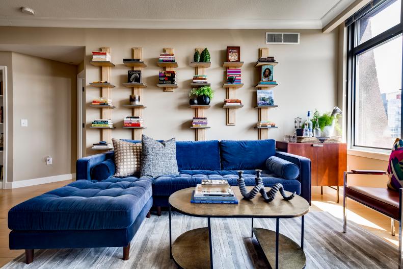 A photo of a living room with a blue sectional and tan bookshelves.