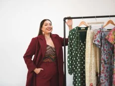 Woman Standing, Smiling With Rack of Dresses