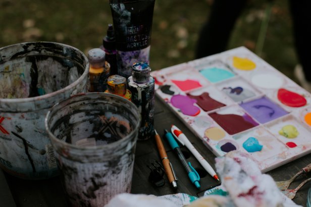 An assortment of artist tools covered in paint sit on a table outside.