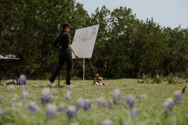 Artist Sarah Kraning looks at her painting in a lush clearing in Texas.