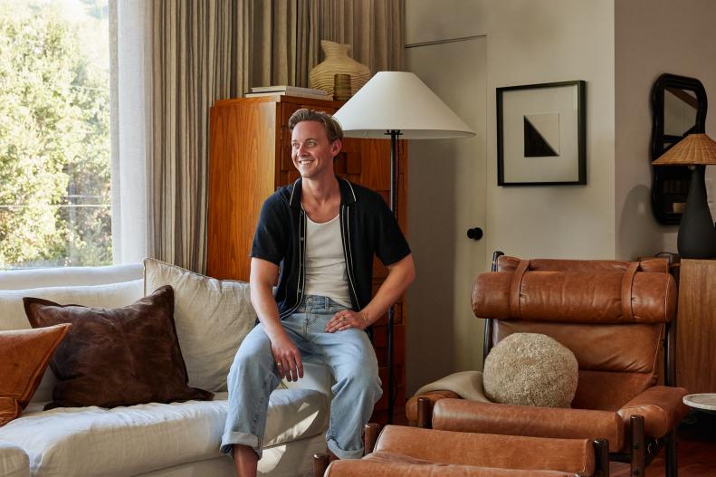 Man Smiles to Camera Seated on White Linen Sofa
