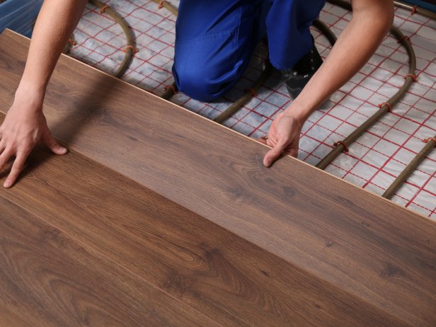 Worker installing new wooden laminate over underfloor heating system, closeup