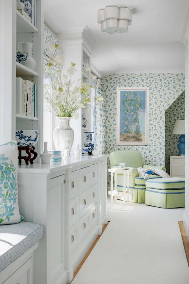 The style of the house is a true 1920's Storybook House which lends itself to being whimsical. Designer, Rhonda Everts took her inspiration from the fairytale architecture and incorporated lots of color and architectural details that are current yet classic. Blue and green is the homeowner’s favorite color combo and it is showcased in unique ways in the various rooms in the home. In the bedroom the blues and greens bring an engaging pattern play that feels light and bright with a clean white backdrop in the bed linens, ceiling and with lots of natural light through the picturesque window seat. The color palette and design details continue into the primary bathroom that enchants with details like the scalloped edges on the custom millwork and mirrors, that adds to the allure of the patterns in the trellis wallpaper and floral fabric on the vanity chair and roman shade window treatments. The living room offers a joyful introduction to the home with glossy green built-in cabinets that offer a compelling backdrop to bold patterned pink fabrics. The myriad of trims and welts add to the luxe and layered look of the space that is designed to bring a smile. A small barrel chinoiserie chair that the homeowner inherited from her mother is raspberry red and inspired the accent colors in the sunroom, and into the bright white kitchen that pops with colorful pendants and boldly patterned window treatments. Bold color with a classic preppy playfulness is in every space, from the outdoor terrace to the wallpapered laundry room. The result is a whimsical storybook of a home!