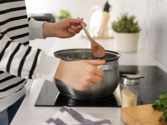 Woman with wooden spoon cooking soup in kitchen, closeup