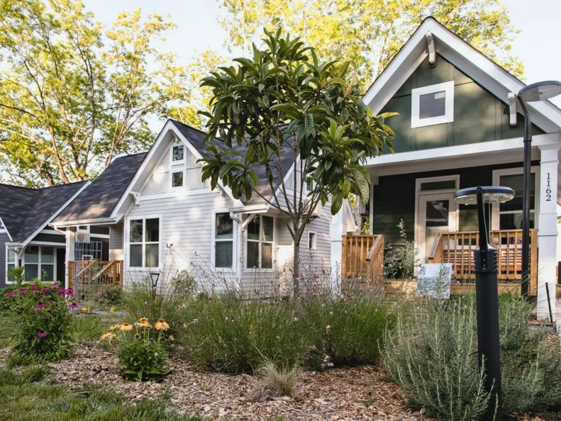 Two houses, side by side, with mulch, flowers and a tree in the front yards.