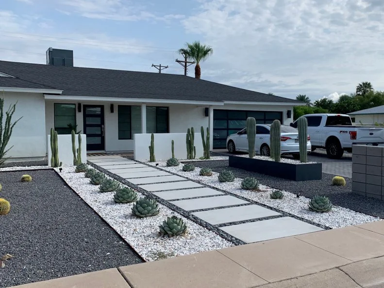 A front yard landscaped with white and dark colored rocks and dry-climate plants
