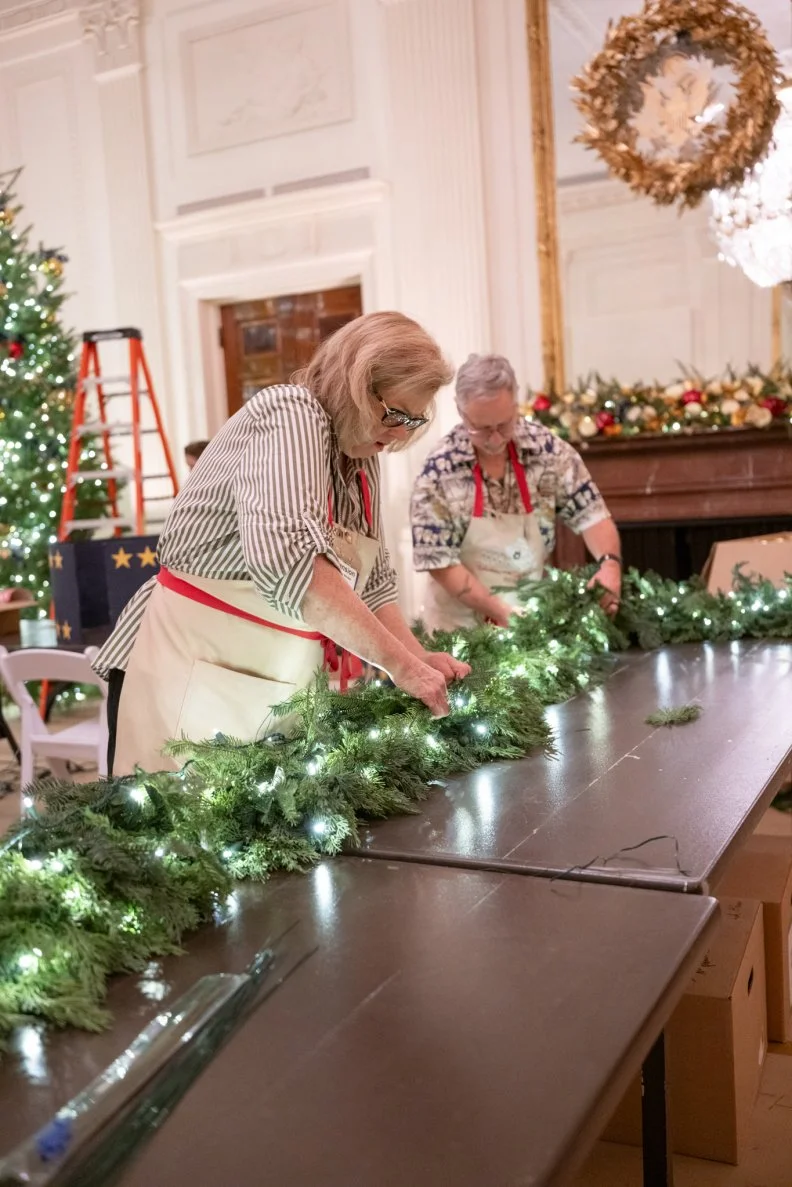 Seven hundred feet of garlands are featured in the White House as part of the 2025 holiday decor. Here volunteers in the East Room add twinkling white lights to a garland.