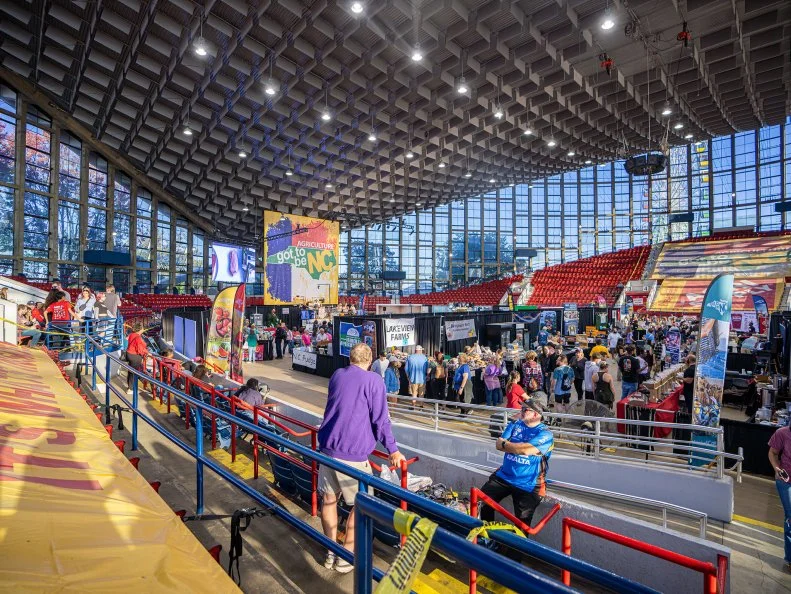 https://www.ncagr.gov/divisions/ncstatefair
In 2024, almost a million visitors attended the North Carolina State Fair, which returns to Raleigh on Oct. 16-26, 2025. The state ranks eighth in the U.S. for agricultural production, and the fair showcases its agriculture and agribusinesses.  Don't miss the Dorton Arena, an architectural landmark, for craft beers, wines and ciders in the  NC Public House; nicknamed the “potato chip,” this arena was the first structure in the world to use a cable-supported roof. Stroll the Village of Yesteryear to see more than 75 artists, potters, weavers, basket makers and other craftspeople demonstrate their skills and sell their items. Before you call it a day, soar above the midway on the State Fair Flyer, a ten-minute chair-lift ride that goes up to to 45 feet high. Part of the fun is getting to the fair if you can ride Amtrak; their trains deposit riders at the gate from Raleigh, Durham, Cary and other locations, and the stop is wheelchair accessible.
https://www.ncagr.gov/divisions/ncstatefair/bookyourevent/dortonarena
https://www.facebook.com/StateFairFlyer/https://www.ncagr.gov/divisions/ncstatefair/2024/attractions/heritagecircle
https://www.ncagr.gov/divisions/ncstatefair/2024/attractions/villageofyesteryear
https://www.ncagr.gov/divisions/ncstatefair/2024/general%20info/parking#NCByTrainAMTRAKTrainService-9315