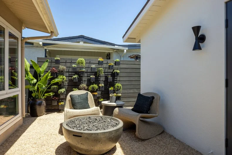 Taking full advantage of the spectacular Los Angeles weather, Drew and Jonathan create an outdoor living space that opens onto the music room and lounge. Ken has long admired a succulent wall in his own home, so John decides he needs to make sure Ken gets one in this lush oasis featuring a pea gravel floor, a stained wood fence and retro outdoor lighting.