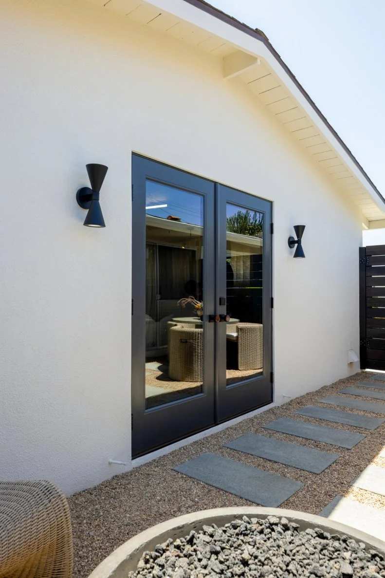 Black frame French doors offer stylish access to the music room from the patio. Drew and Jonathan strike a contemporary vibe with two midcentury-reminiscent outdoor sconces and oversized pavers laid between pea gravel on the patio surface.