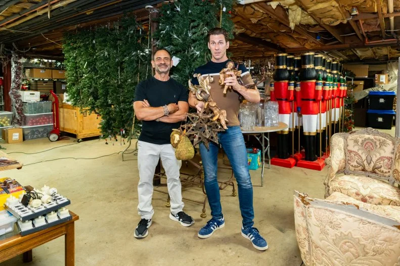 Homeowners Dominick Marangi and Matt Tumminello  pose in the basement storage space featuring various Christmas decorations, as seen on Holiday Hoarders, Season 1.